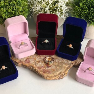 May include: Five velvet ring boxes in pink, red, blue, and navy blue. Each box contains a silver ring with a pink opal gemstone.