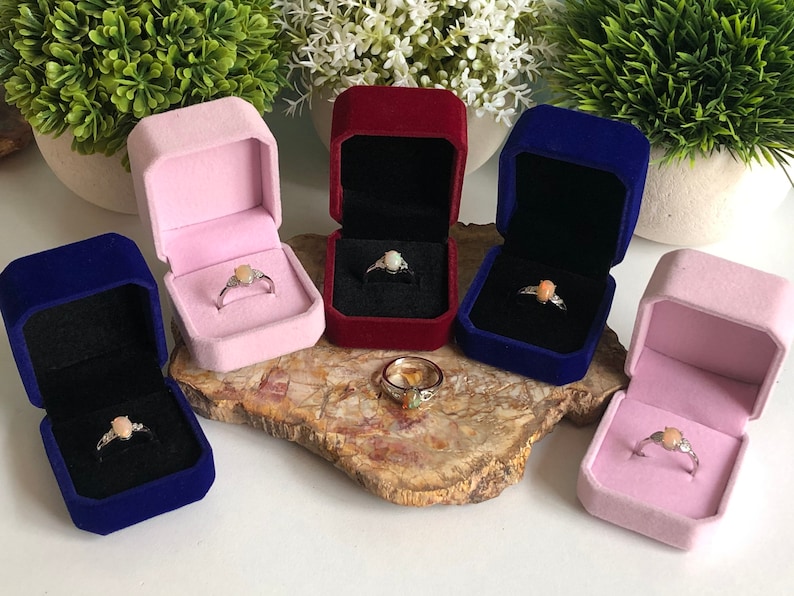 May include: Five velvet ring boxes in pink, red, blue, and navy blue. Each box contains a silver ring with a pink opal gemstone.