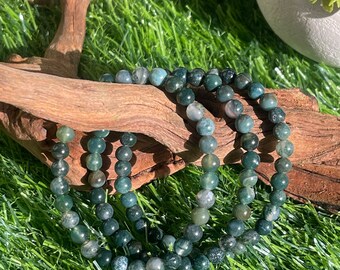 May include: A green agate beaded bracelet with multiple strands of beads. The bracelet is on a wooden surface with green grass in the background.