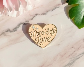 Gold- und orangefarbene Emaille-Herzbrosche mit der Aufschrift „Mehr Selbstliebe“. Ein Accessoire für Wohlbefinden und mentale Gesundheit. Ein positives Geschenk. Ein charmanter, süßer und femininer Stil.