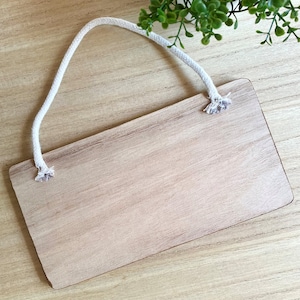 Puede incluir: Un letrero rectangular de madera con un acabado marr&oacute;n claro y una cuerda blanca para colgar. El letrero tiene esquinas redondeadas y un aspecto natural de veta de madera. La cuerda est&aacute; sujeta en la parte superior.