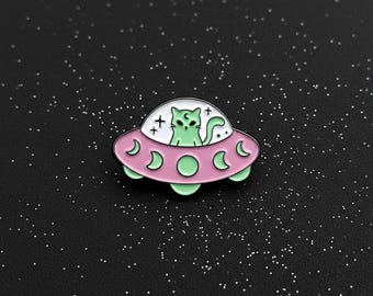 Pin de esmalte negro con colores pastel, diseño de platillo volador con gato.