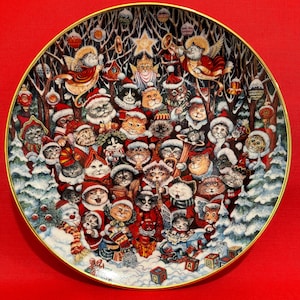 May include: A Christmas-themed ceramic plate depicting a festive scene of cats dressed in Santa hats and other holiday attire. The cats are gathered around a Christmas tree, singing carols and playing instruments. The plate is decorated with a gold rim and a snowy winter scene.