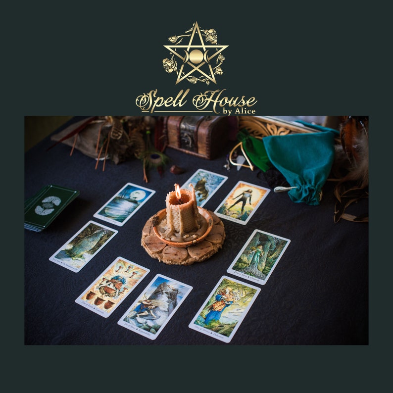 May include: A tarot card reading spread with nine cards laid out on a dark surface. A lit candle sits in the center of the spread. The cards are surrounded by various objects, including a small wooden box, a green pouch, and feathers.