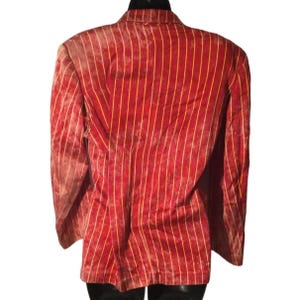 Op de afbeelding: Een rode blazer met verticale gele strepen. De blazer heeft een klassiek ontwerp met een reverskraag en lange mouwen. De stof lijkt fluweel of een vergelijkbaar zacht materiaal te zijn. De blazer wordt van achteren getoond.