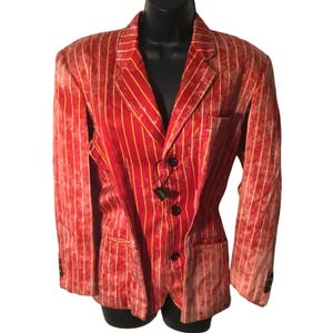 Op de afbeelding: Een rode blazer met gele verticale strepen. De blazer heeft drie zwarte knopen en een revers met inkeping. De stof heeft een getextureerde uitstraling. De blazer wordt gepresenteerd op een zwarte mannequin.