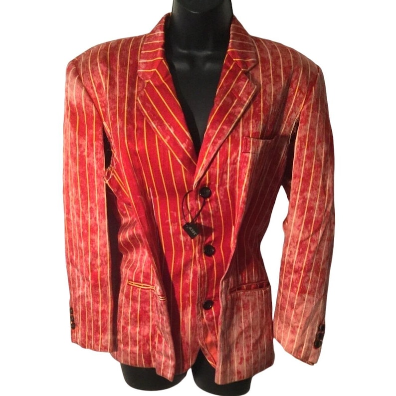 Op de afbeelding: Een rode blazer met gele verticale strepen. De blazer heeft drie zwarte knopen en een revers met inkeping. De stof heeft een getextureerde uitstraling. De blazer wordt gepresenteerd op een zwarte mannequin.