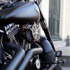 May include: Close-up of a black motorcycle engine with chrome accents. The engine has a large air filter with a black and silver design. The motorcycle is parked on a brick surface.