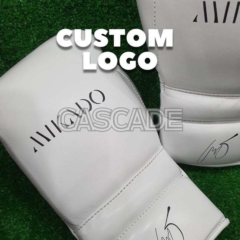 Peut inclure: Une paire de gants de boxe blancs avec du texte noir qui dit "CUSTOM LOGO" et "AIIIDO CASCADE".