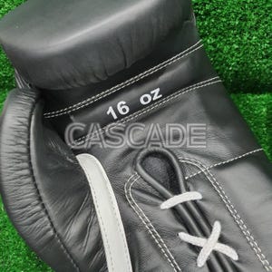 Peut inclure: Gants de boxe en cuir noir avec des coutures blanches et une &eacute;tiquette blanche indiquant "16 OZ CASCADE".
