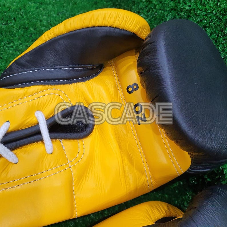 Peut inclure: Une paire de gants de boxe jaunes et noirs avec des lacets blancs. Les gants ont un patch en cuir noir sur le c&ocirc;t&eacute; avec le num&eacute;ro "8 OZ" imprim&eacute; dessus.