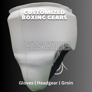 May include: White leather groin protector with black straps and the text "CUSTOMIZED BOXING GEARS" and "CASCADE" on the front. The text "Gloves | Headgear | Groin" is printed below the protector.