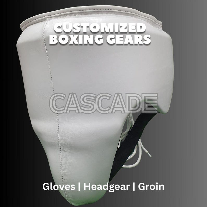 May include: White leather groin protector with black straps and the text "CUSTOMIZED BOXING GEARS" and "CASCADE" on the front. The text "Gloves | Headgear | Groin" is printed below the protector.