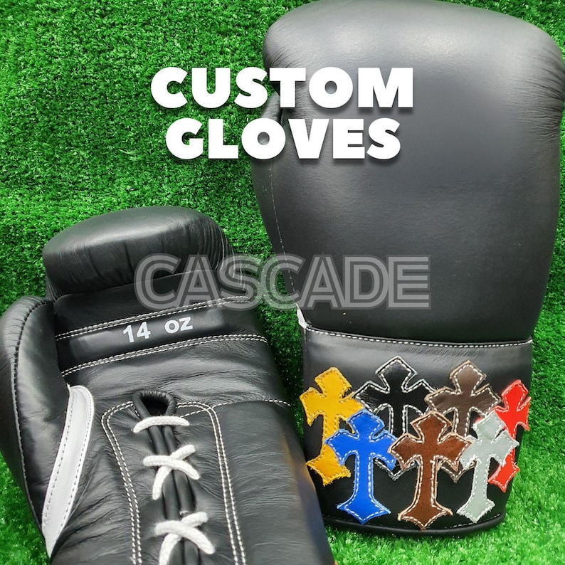 K&ouml;nnte beinhalten: Schwarze Boxhandschuhe mit wei&szlig;en N&auml;hten und farbenfrohen Kreuzdesigns. Die Handschuhe sind mit "14 oz" beschriftet, und die Texte "CUSTOM GLOVES" und "CASCADE" sind sichtbar.