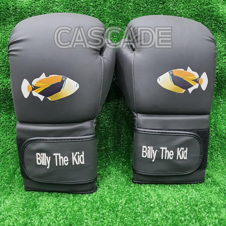 May include: A pair of black boxing gloves with a white fish design and the text "Billy The Kid" on the wrist strap. The gloves have the word "CASCADE" printed on the top.