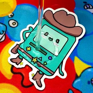 May include: A teal sticker featuring a cartoon character in a cowboy hat and boots. The character has a screen face with a smiling expression. The sticker has a white border and is on a colorful background.