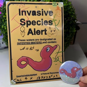May include: A yellow sign with the text "Invasive Species Alert" and a cartoon worm illustration. The sign also includes the text "Infested Waters" and "Contain TheCreatures department". A round button with the same worm illustration is also visible.