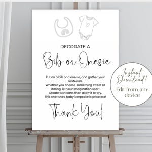 Op de afbeelding: Een wit bord op een houten ezel met de tekst "DECORATE A Bib or Onesie". Het bord bevat lijntekeningen van een slabbetje en een onesie. De woorden "Instant Download!" staan in een cirkel.