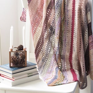 May include: A multi-colored knitted shawl with a lacy pattern draped over a white chair. The shawl has stripes of pink, purple, brown, and green.
