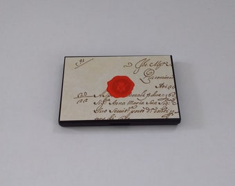 May include: A vintage-style, rectangular, wooden box with a hinged lid. The lid is decorated with a wax seal and handwritten text in brown ink. The text reads: "192, 2, J.C. Mza, sul comino, Mice, meralis dua=362, Sig: Anna Maria Sua Sig:, Quo Venit, Semis porre de conti, tore di ale."