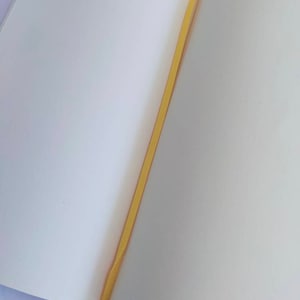 May include: A blank, white notebook with a yellow ribbon bookmark. The notebook is open to a blank page.