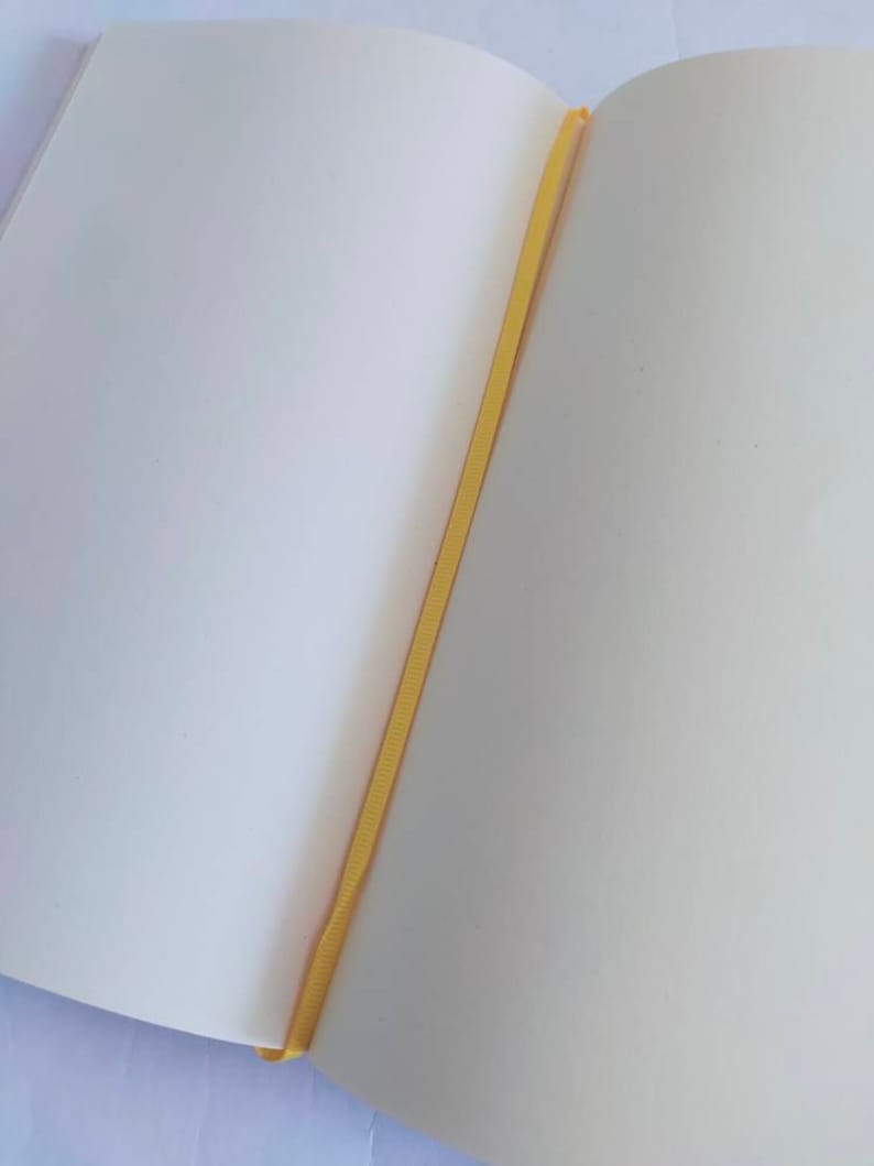 May include: A blank, white notebook with a yellow ribbon bookmark. The notebook is open to a blank page.