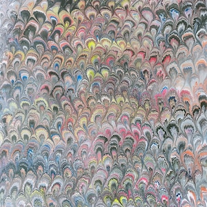 May include: A close-up of a decorative paper with a marbled pattern. The design features a repeating, fan-like motif in shades of gray, black, pink, yellow, and blue. The overall effect is a textured, colorful, and artistic design.