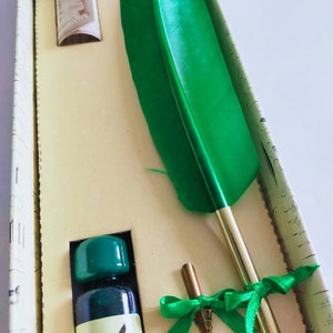 Op de afbeelding: Een groene veerpenset in een doos met een flesje groene inkt, twee penpunten en een rol papier. Het etiket van de inktfles is "inchiostro Verde Made in Italy".