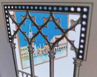 Puede incluir: Una artesanía de papel con una ventana recortada que muestra una escena de una ciudad con edificios y agua. La ventana está enmarcada por un diseño de celosía en blanco y negro.
