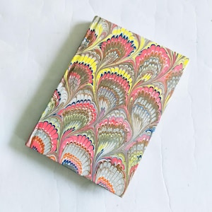 May include: A small notebook with a colorful marbled cover featuring a peacock feather design in shades of pink, yellow, blue, and brown.
