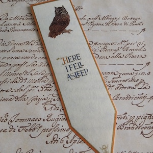 May include: A brown and white owl bookmark with a gold border. The bookmark has the text "HERE I FELL ASLEEP" written on it.