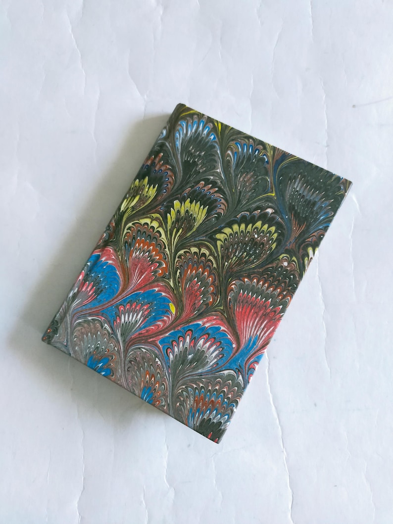 May include: A small, colorful notebook with a marbled cover. The cover features a swirling pattern of blue, red, green, and yellow.