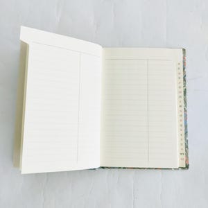 May include: An open notebook with lined pages and a colorful marbled cover. The cover has a small index with letters of the alphabet along the edge.