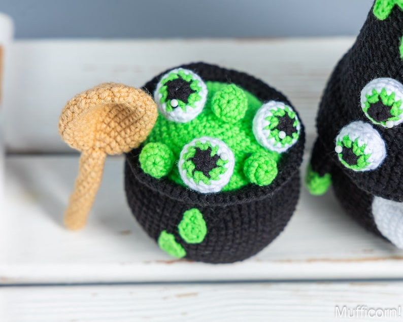 May include: A crocheted cauldron with green goo and googly eyes, a crocheted spoon, and a crocheted black and white monster with googly eyes.