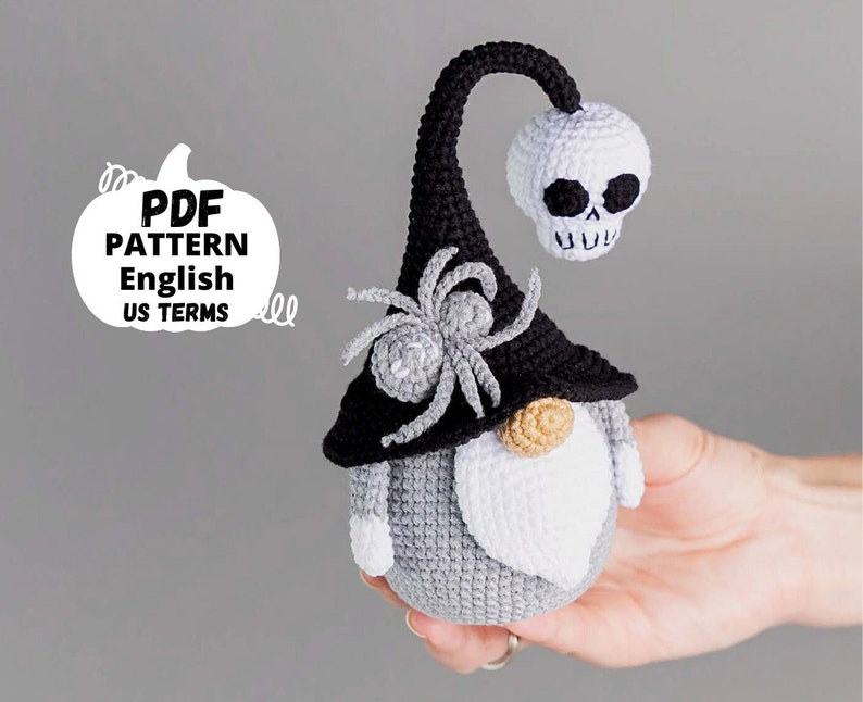 May include: A crocheted Halloween gnome with a black hat, a spider on the hat, and a white skull on top. The gnome has a white beard and a gray body.