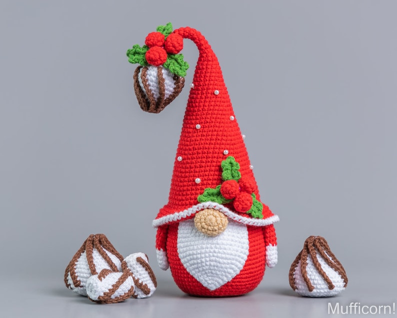 May include: A crocheted Christmas gnome with a red hat, white beard, and a green holly sprig with red berries. The gnome is surrounded by three white and brown crocheted candy canes.