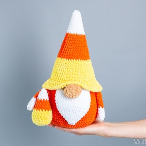 May include: A crocheted candy corn gnome with a white beard and orange, yellow, and white striped hat.