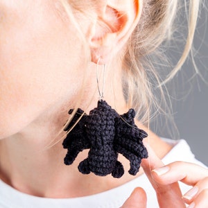 May include: Black crocheted bat earrings hanging from silver hooks. The earrings are dangling from a person's ear.