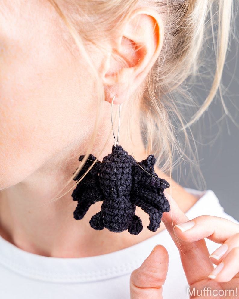 May include: Black crocheted bat earrings hanging from silver hooks. The earrings are dangling from a person's ear.