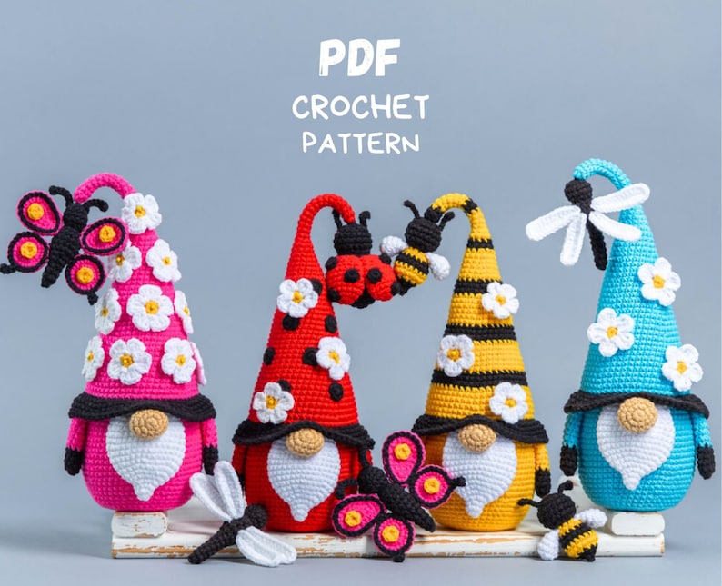 May include: Four crocheted gnomes with different colored hats and insect decorations. The gnomes are wearing white beards and have black eyes. The hats are decorated with white flowers. The gnomes are sitting on a white wooden surface. The text "PDF CROCHET PATTERN" is at the top of the image.