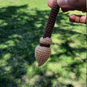 May include: A small crocheted broom with a brown handle and a beige bristle head.