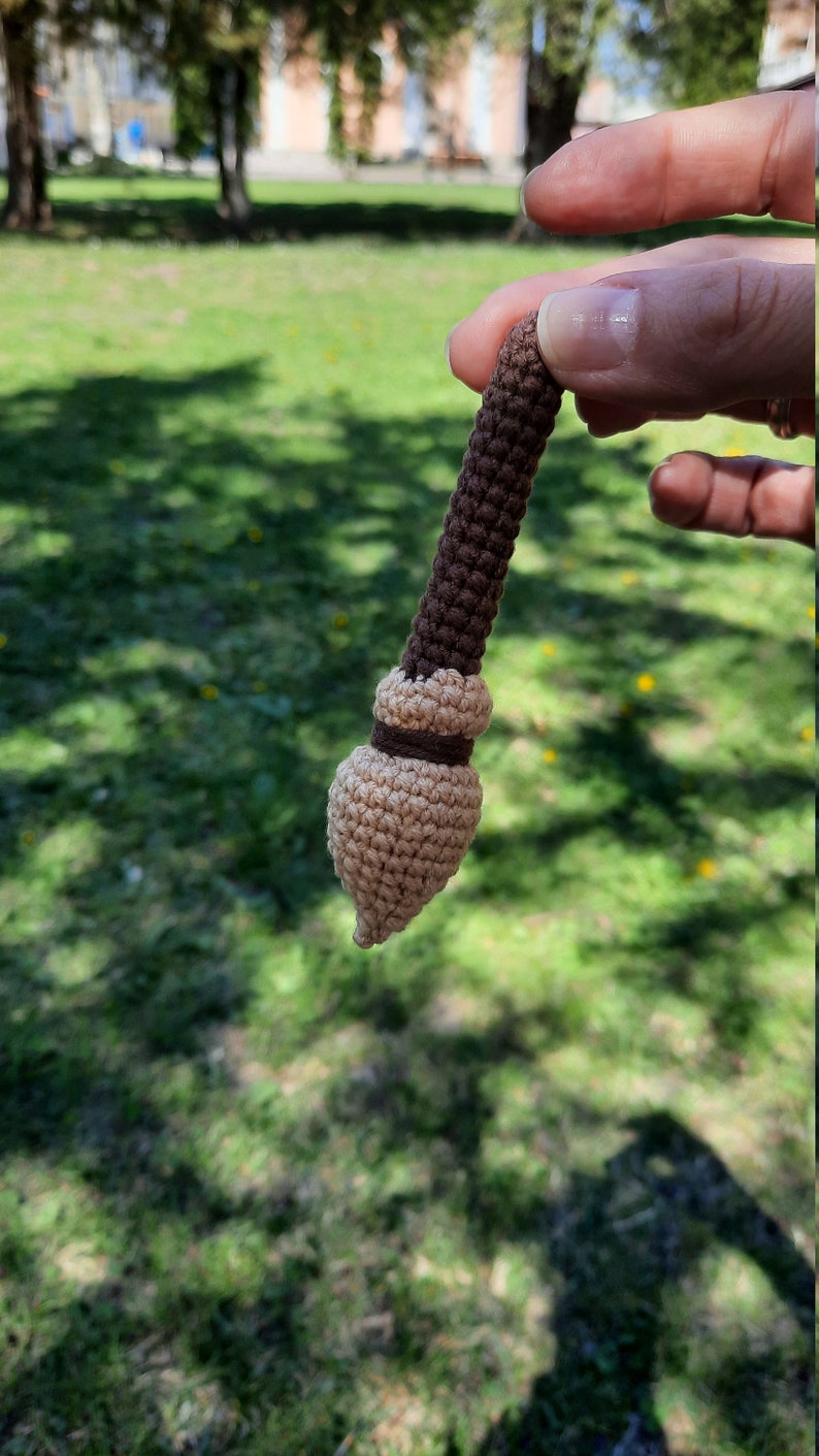 May include: A small crocheted broom with a brown handle and a beige bristle head.