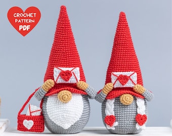 May include: Two crocheted gnomes holding red envelopes with hearts on them. The gnome on the left is carrying a red bag with a white heart on it. The gnomes are wearing red hats and have white beards.