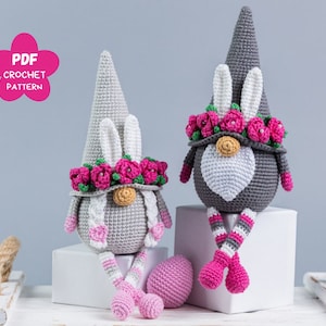 Puede incluir: Dos gnomos de crochet grises con coronas de flores rosas y orejas de conejo blancas. Los gnomos están sentados en superficies blancas. Un gnomo está sentado con las piernas cruzadas y el otro gnomo está sentado con las piernas estiradas hacia adelante.  PDF CROCHET PATTERN.