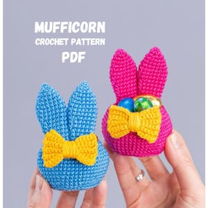 Może przedstawiać: Dwa szydełkowe koszyczki w kształcie króliczków, jeden niebieski i jeden różowy, każdy z żółtymi kokardkami. Różowy króliczek trzyma kolorowe pisanki. U góry tekst "MUFFICORN CROCHET PATTERN PDF". Idealne na Wielkanoc.