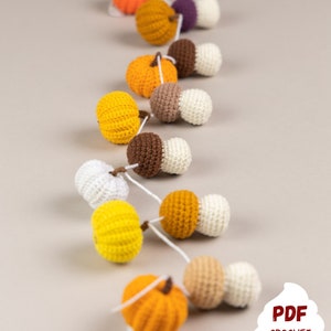 May include: A crocheted garland with alternating orange pumpkins and brown and white mushrooms. The garland is strung together with white yarn. The garland is on a light gray background. The text "PDF CROCHET PATTERN MUFFICORN" is at the bottom of the image.