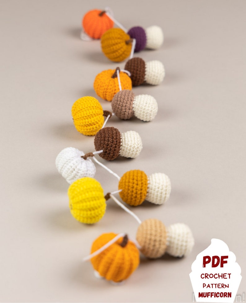 May include: A crocheted garland with alternating orange pumpkins and brown and white mushrooms. The garland is strung together with white yarn. The garland is on a light gray background. The text "PDF CROCHET PATTERN MUFFICORN" is at the bottom of the image.