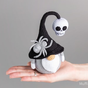 May include: A gray and white crocheted gnome wearing a black witch hat with a spider and a white skull on top.