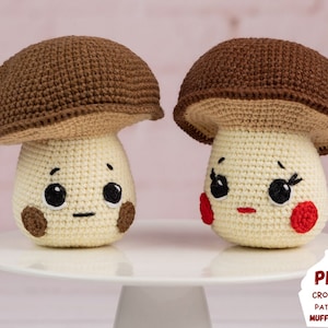 Puede incluir: Dos peluches de champiñón tejidos a crochet con sombreros marrones y cuerpos blancos. Los champiñones tienen ojos y bocas bordados, y uno tiene mejillas rojas.