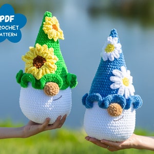 May include: Two crocheted gnomes with white bodies, one with a green hat with a yellow sunflower and the other with a blue hat with a white daisy.